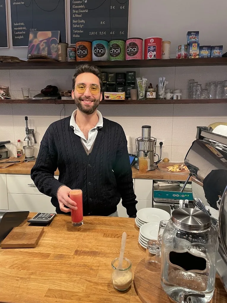 Sami hinter der Theke im Café Frida, lächelnd, mit einem Drink in der Hand